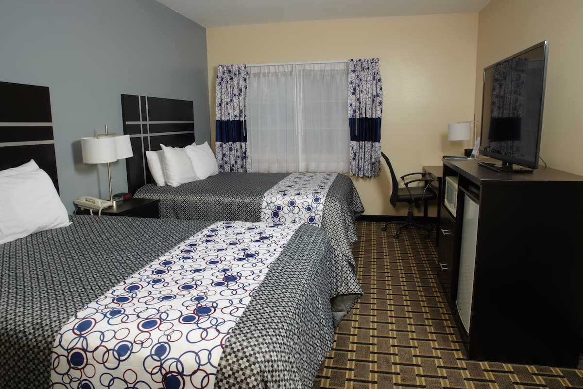 A hotel room with two beds, a desk, a TV, and a chair.