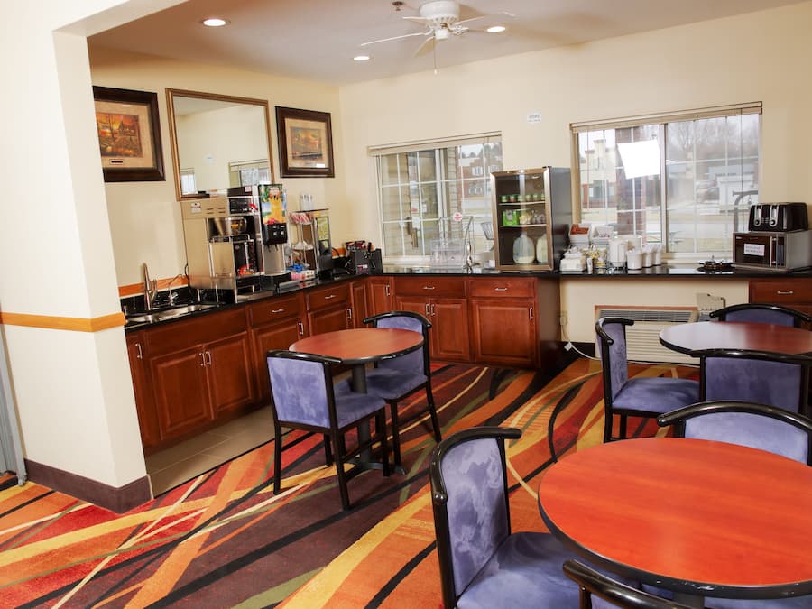 A hotel room with a kitchenette, a dining area with four chairs and a table, and a large window with a view of the outside.