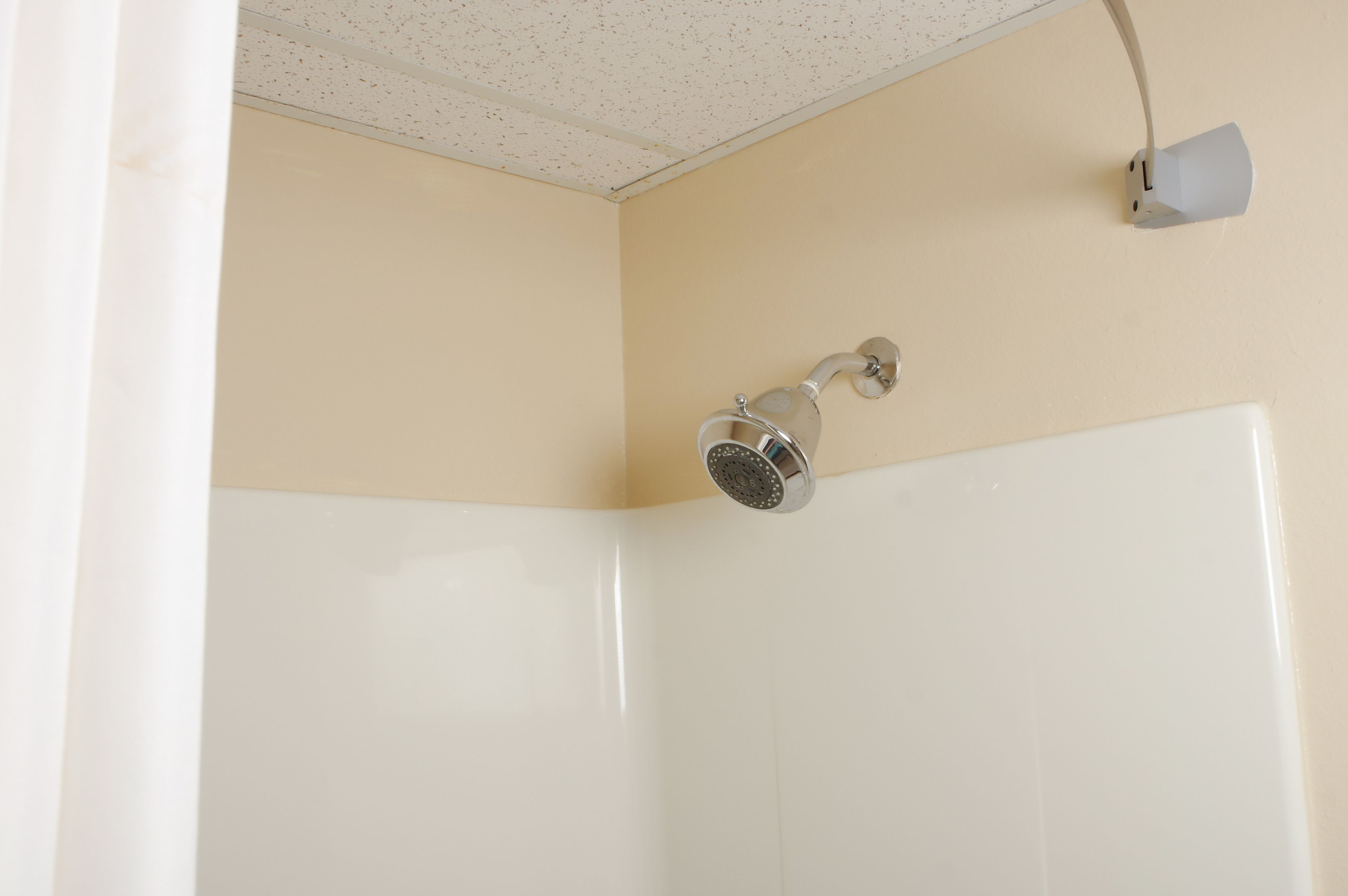A corner of a room with a shower head mounted on the wall, a light fixture, and a white tiled wall.