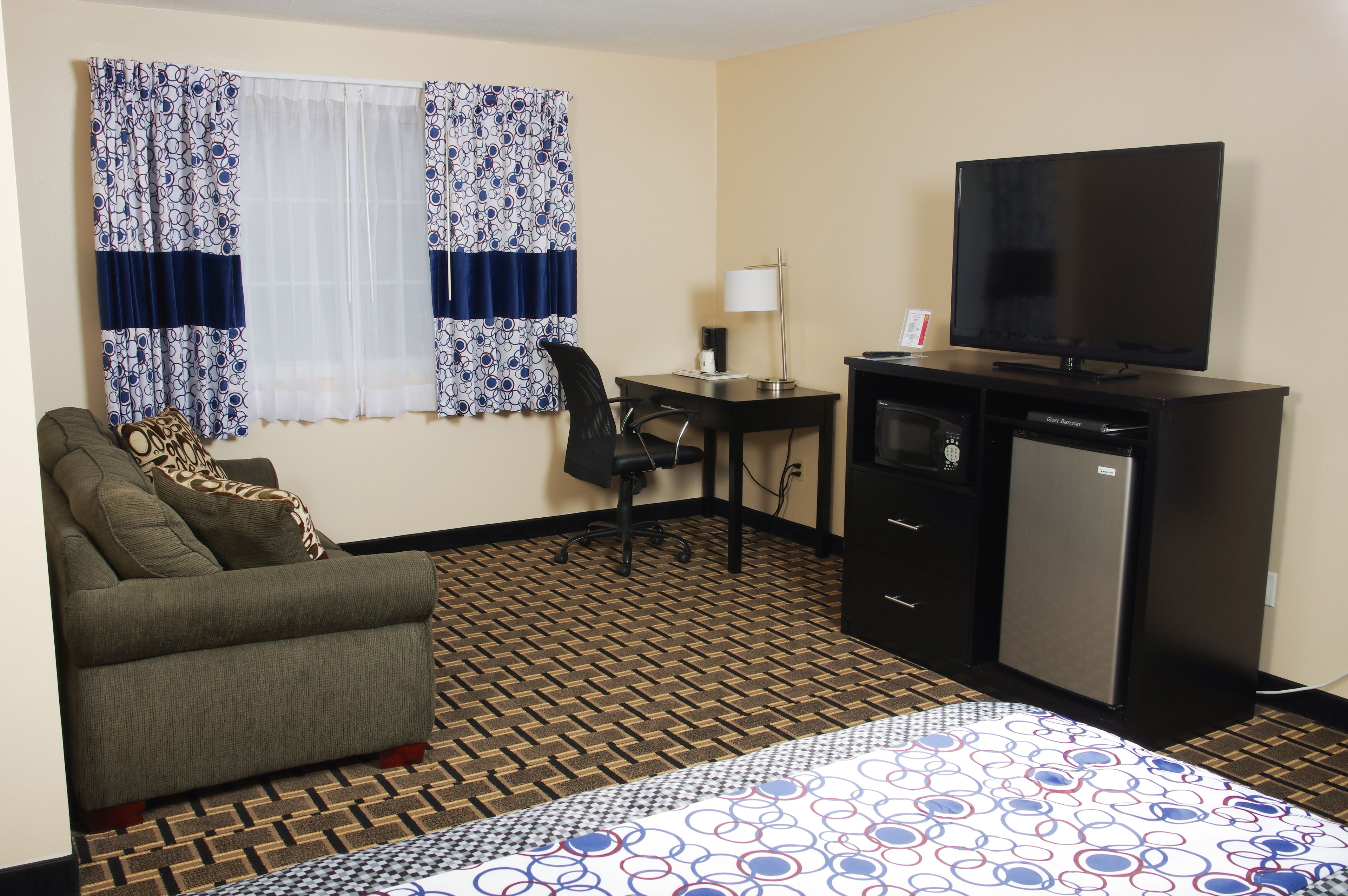 A hotel room with a bed, a desk, a chair, a television, and a refrigerator.