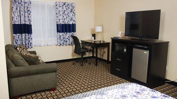 A hotel room with a bed, a desk, a chair, a television, and a refrigerator.