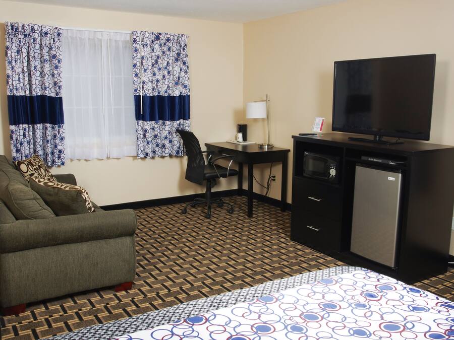 A hotel room with a bed, a desk, a chair, a television, and a refrigerator.