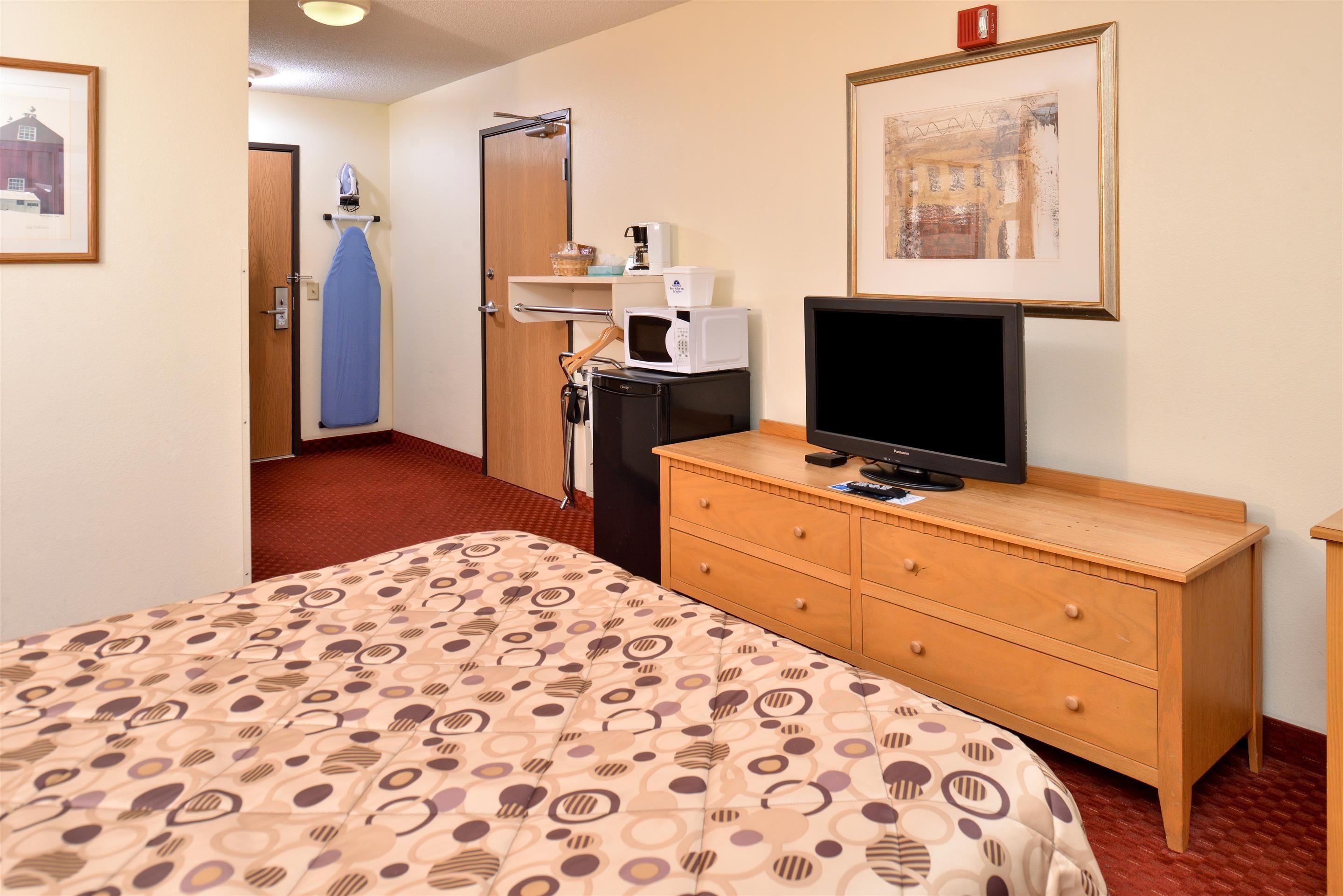 Habitación de hotel con cama, cómoda de madera, televisor, microondas y puerta que da a otra habitación.