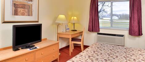 A hotel room with a bed, a desk with a chair, a television, a framed picture, and a window with curtains.