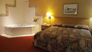 A hotel room with a large bed, a separate bathroom with a bathtub, a bedside table with a lamp, and a framed picture on the wall. - Americas Best Value Inn & Suites Spring Valley (Spring Valley)