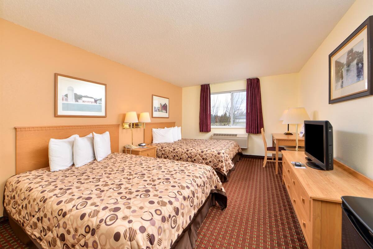 A hotel room with two beds, a desk, a television, and framed pictures on the walls.