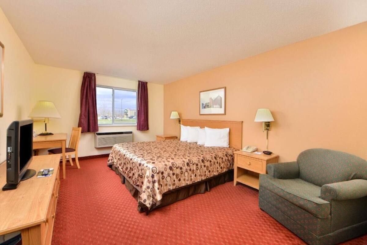 A hotel room with a bed, a desk, a chair, a television, and a window with curtains.