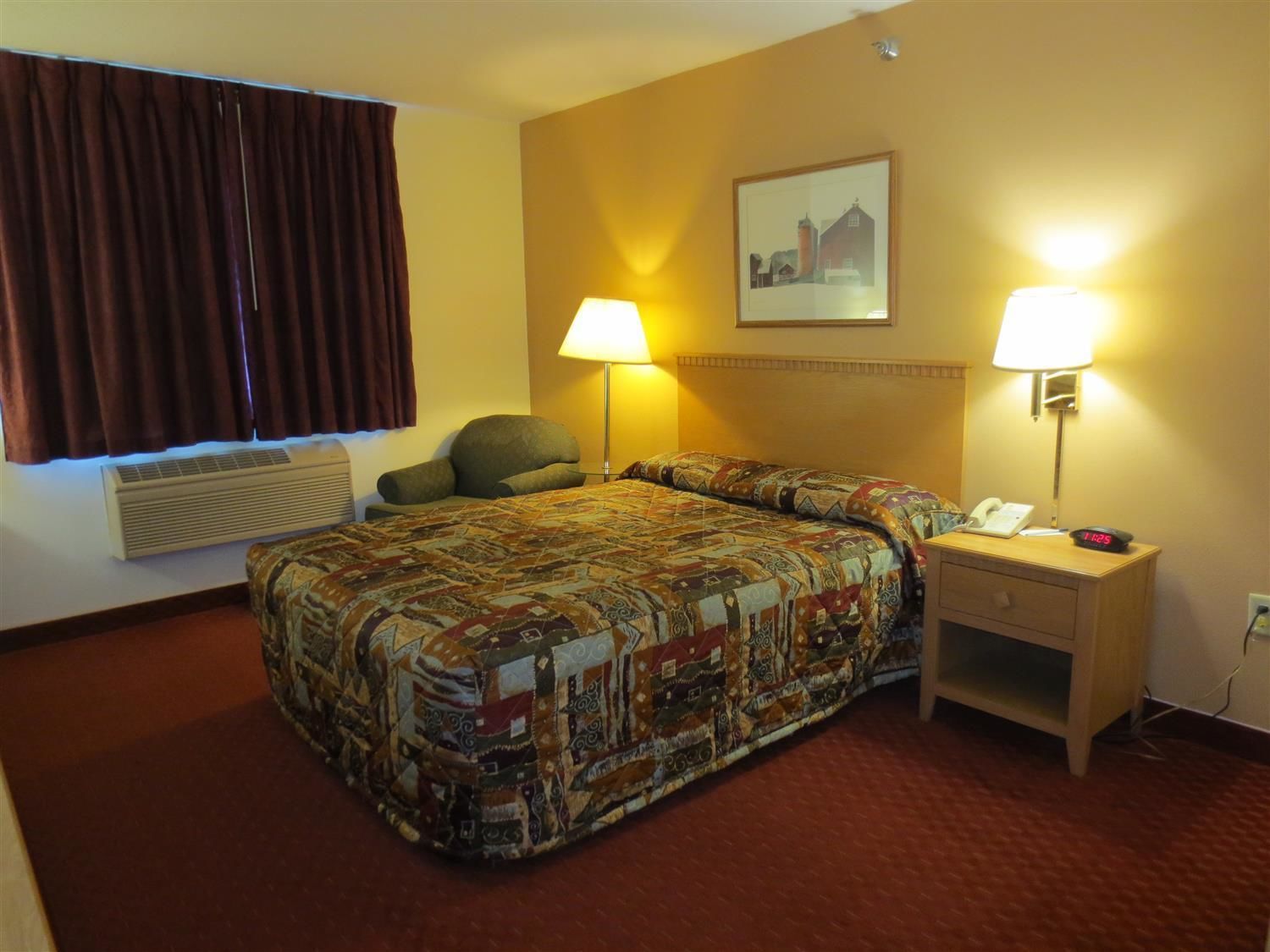 Habitación de hotel con una cama grande, dos lámparas de noche, una silla, un escritorio con teléfono y un cuadro en la pared.