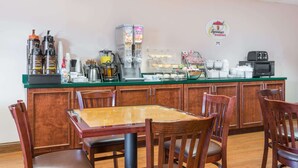 A breakfast bar with coffee makers, a blender, and a cereal dispenser. There are wooden chairs and a table. - Super 8 by Wyndham Grayson (Grayson)