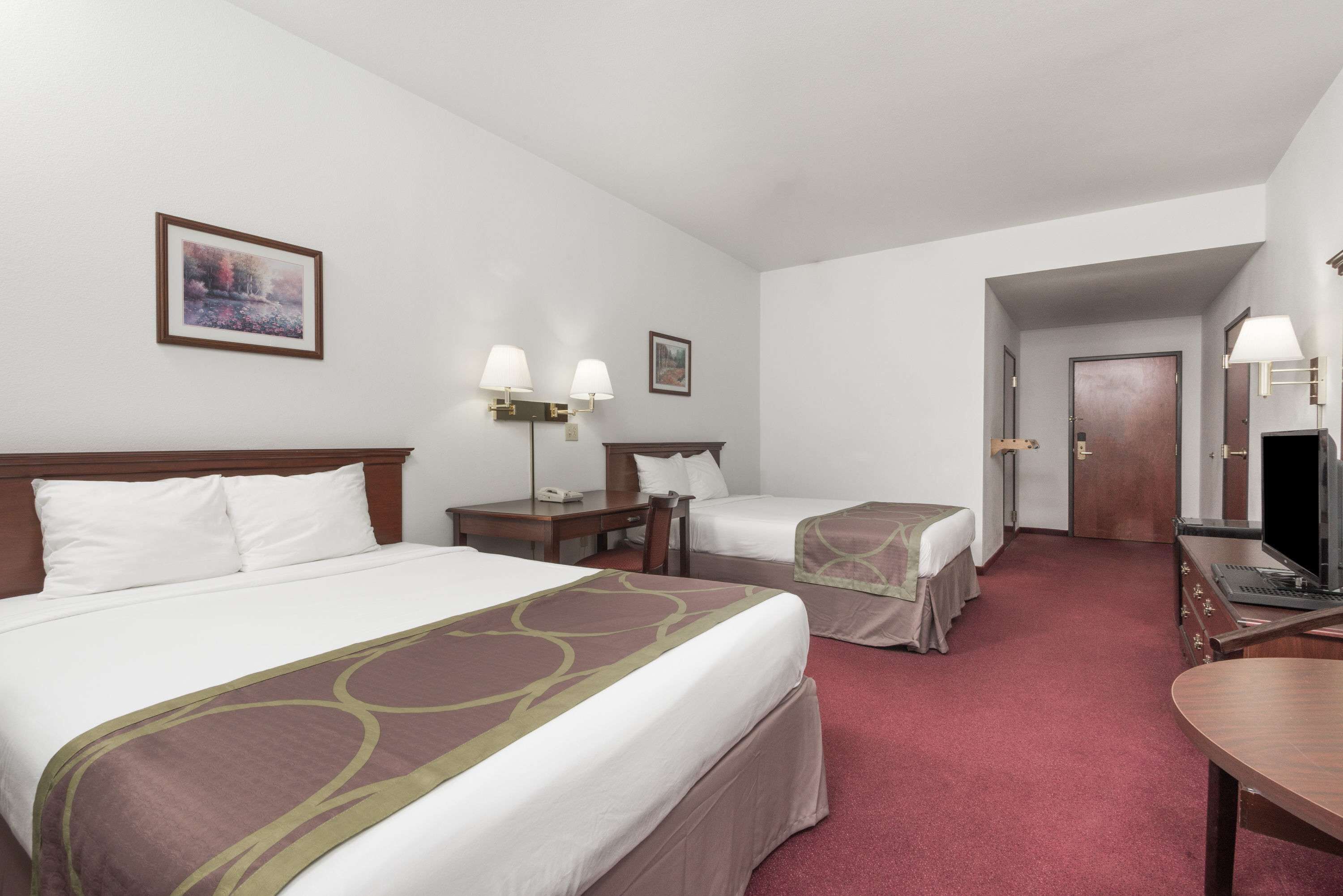 A hotel room with two beds, a desk, a chair, a TV, and a door leading to another room.