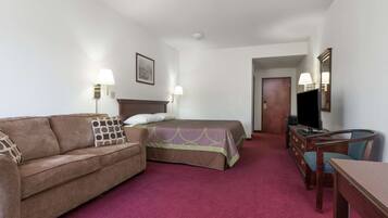 Una habitación de hotel con cama, sofá, televisión, cómoda y escritorio.