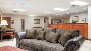 A lobby with a leather sofa, a wooden reception desk, a clock, and a framed picture on the wall. - Super 8 by Wyndham Grayson (Grayson)