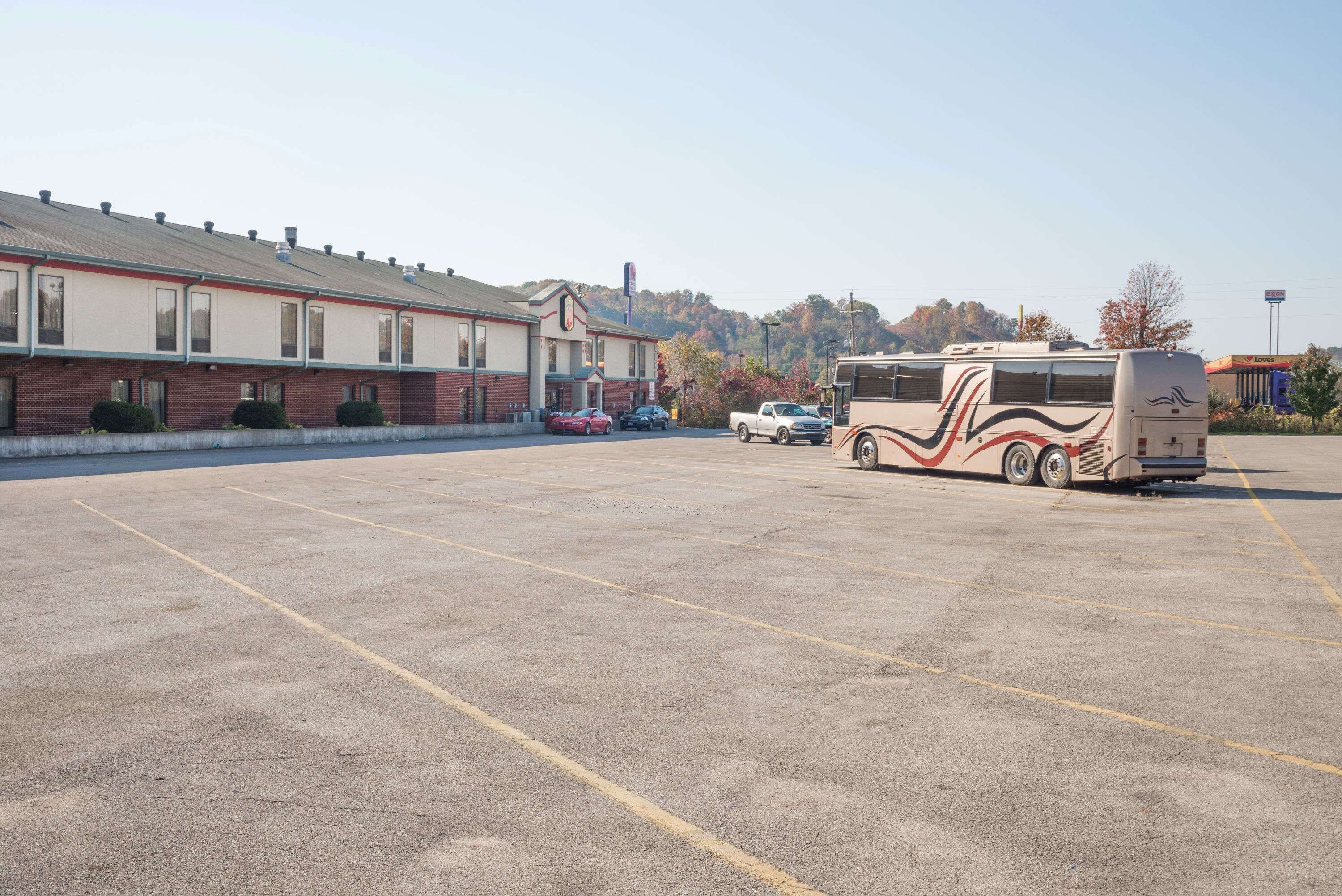A parking lot with a large RV and a few cars. There is a building with a red brick facade and a sign on the roof.