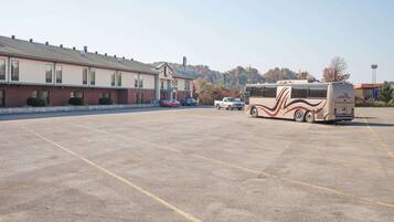 A parking lot with a large RV and a few cars. There is a building with a red brick facade and a sign on the roof.