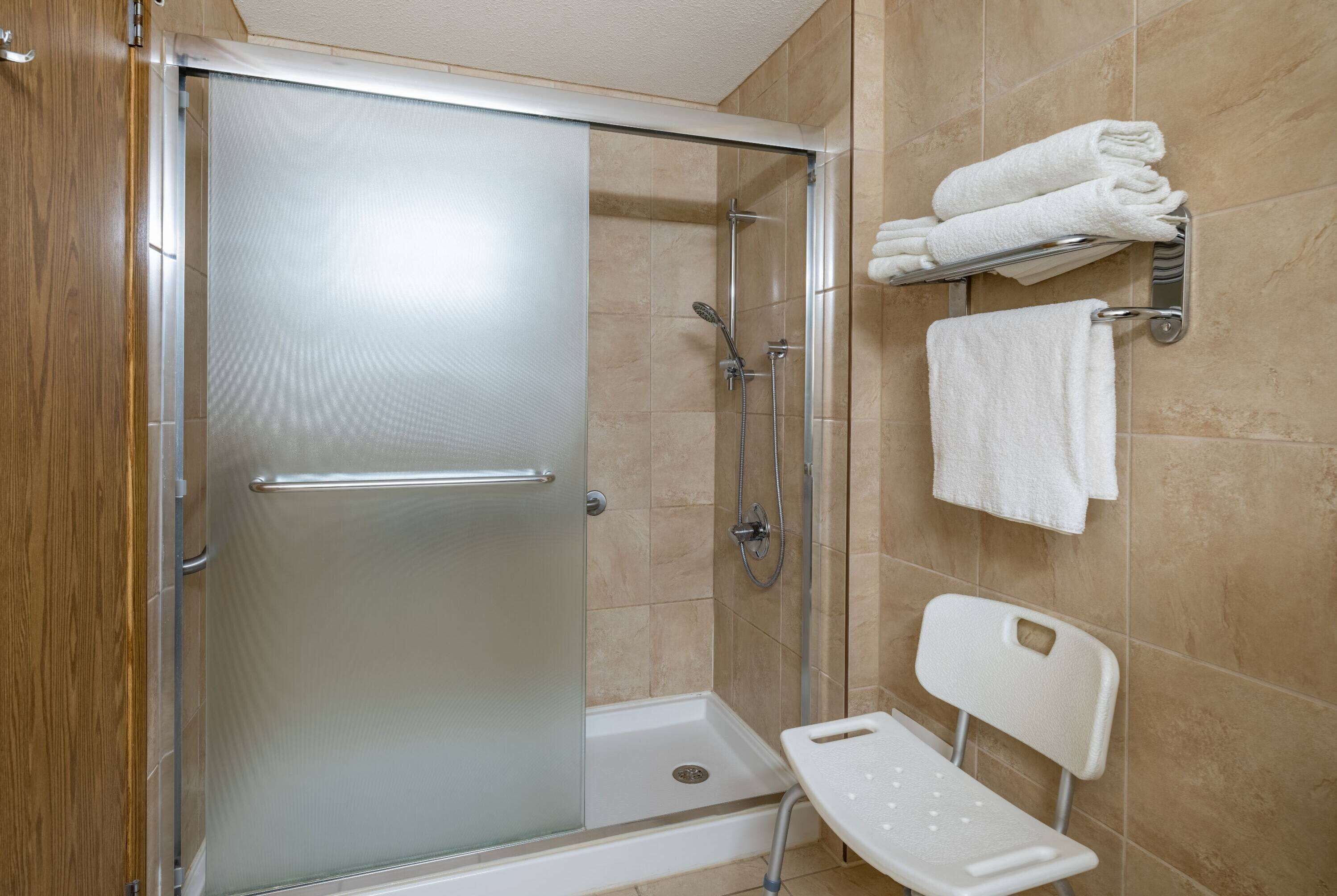 Un área de ducha con puerta de vidrio, un perchero blanco con toallas y una silla blanca.
