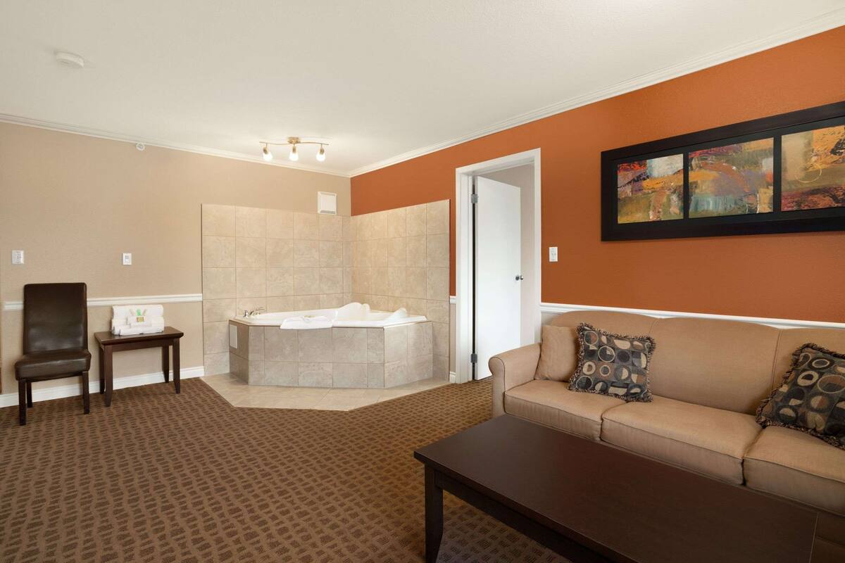 Una sala de estar con un sofá beige, un sillón marrón, una mesa de centro y un cuadro grande en la pared.