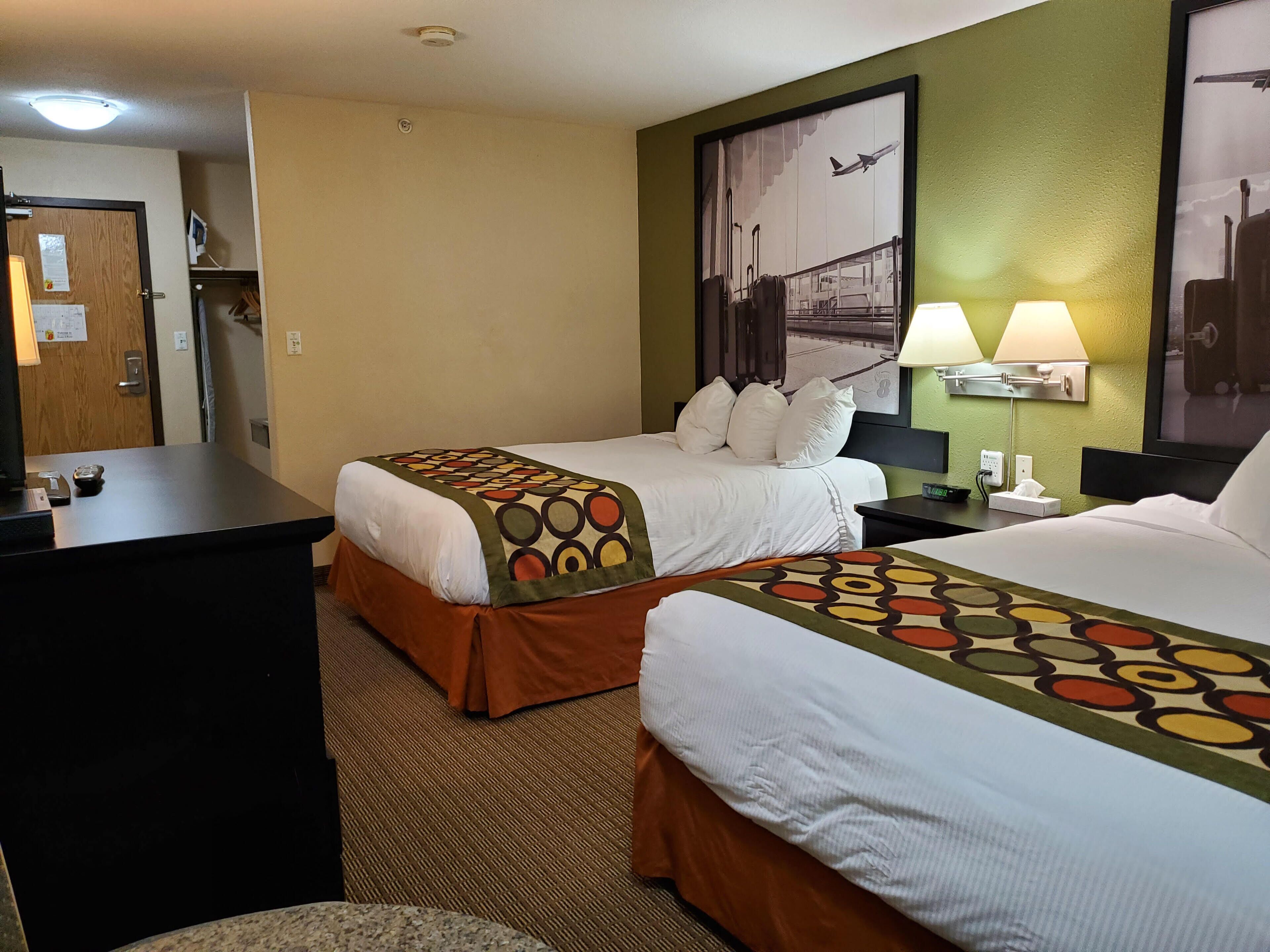 A hotel room with two beds, a desk, and a nightstand with lamps.