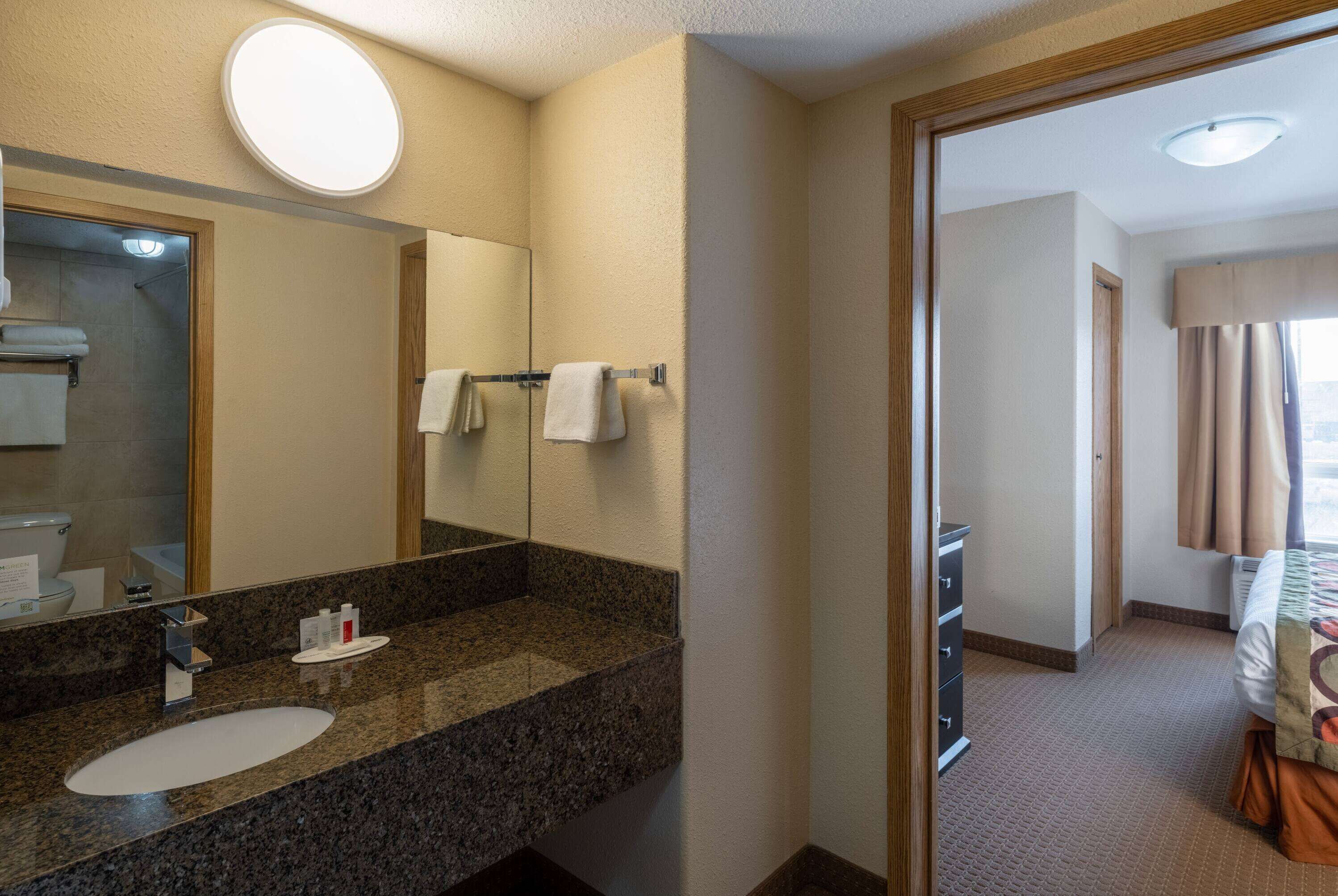 A hotel bathroom with a granite countertop sink, a large mirror, and a towel rack.