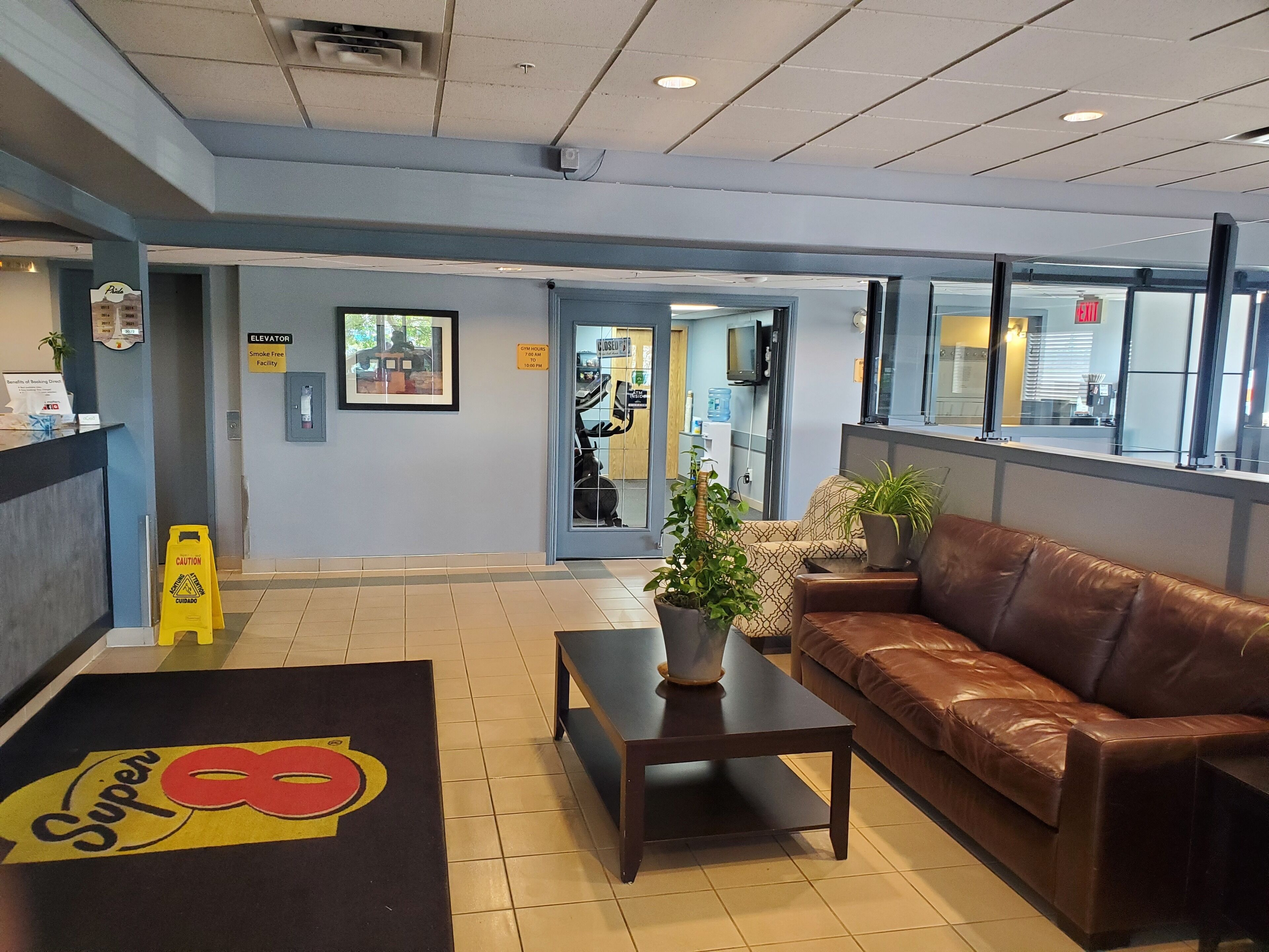 A hotel lobby with a reception desk, a brown leather couch, a coffee table, and a potted plant.