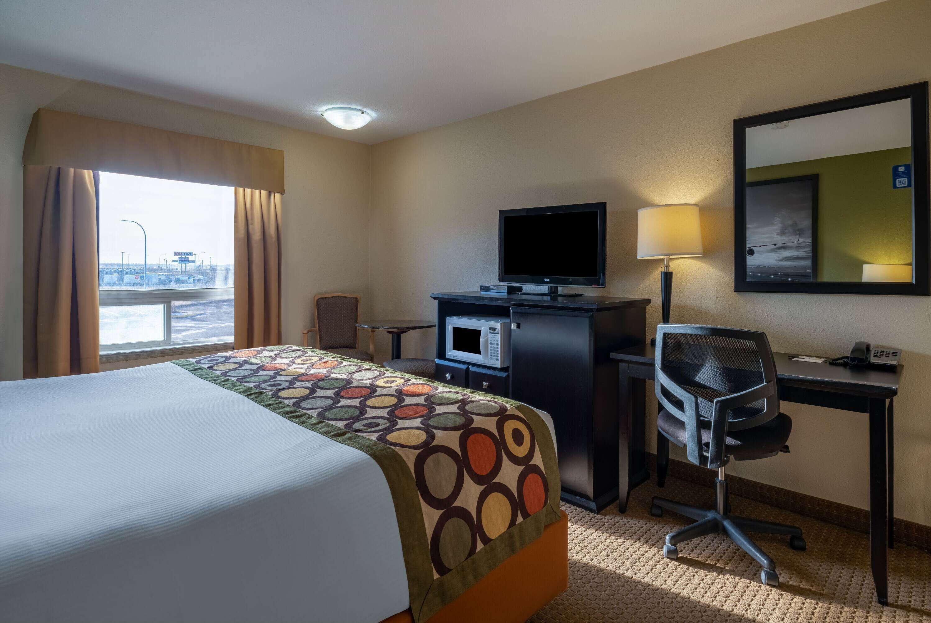 A hotel room with a bed, a desk with a computer, a television, a microwave, and a chair.