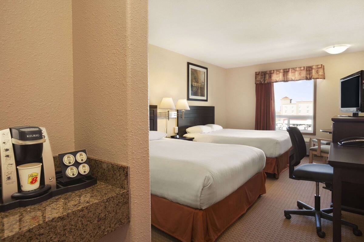 Una habitación de hotel con dos camas, un escritorio, una silla, un televisor y una cafetera.