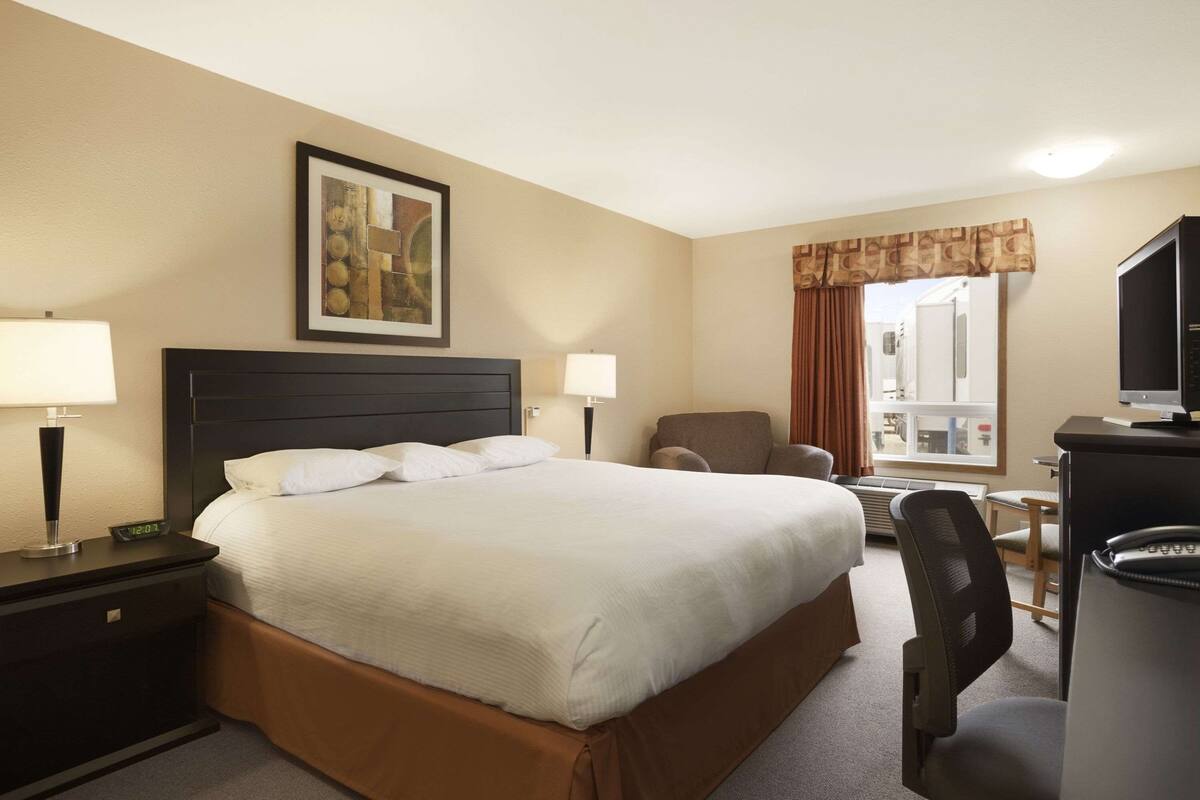 Habitación de hotel con una cama grande, dos mesitas de noche con lámparas, un escritorio con computadora, una silla y una ventana con cortinas.