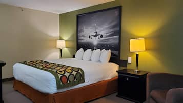 Une chambre d’hôtel avec un grand lit, deux tables de chevet avec des lampes, une chaise et une œuvre d’art représentant un avion, accrochée au mur.