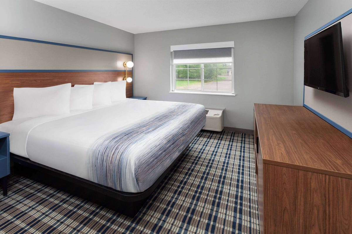 Hotelkamer met een groot bed, een houten hoofdeinde, een flatscreen televisie, een raam en een geruit vloerkleed.