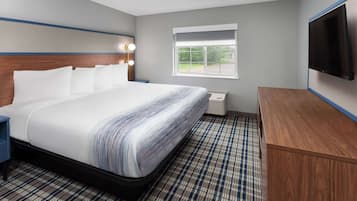 A hotel room with a large bed, a wooden headboard, a flat-screen TV, a window, and a checkered floor.