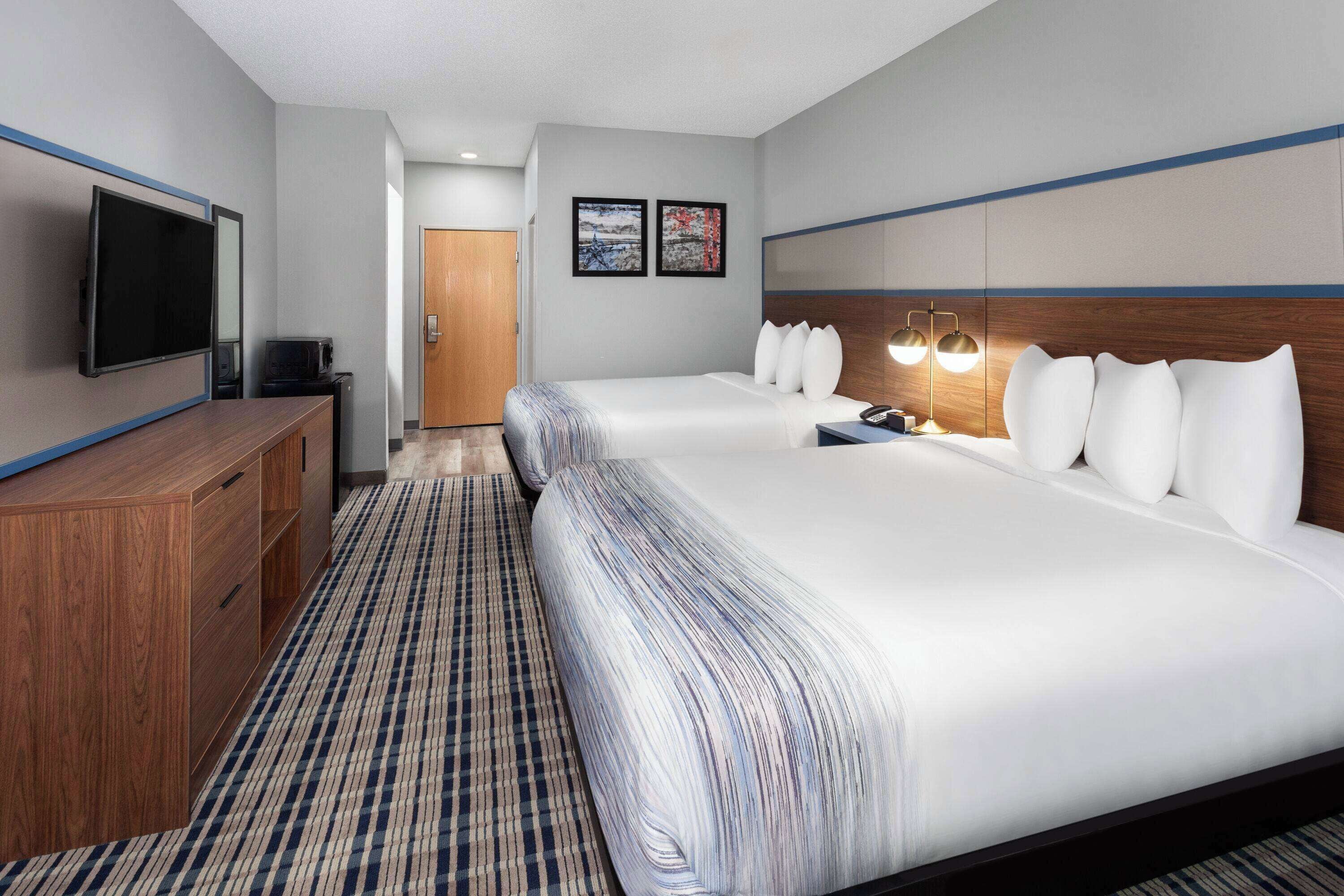 A hotel room with two beds, a TV, a desk, and a door.