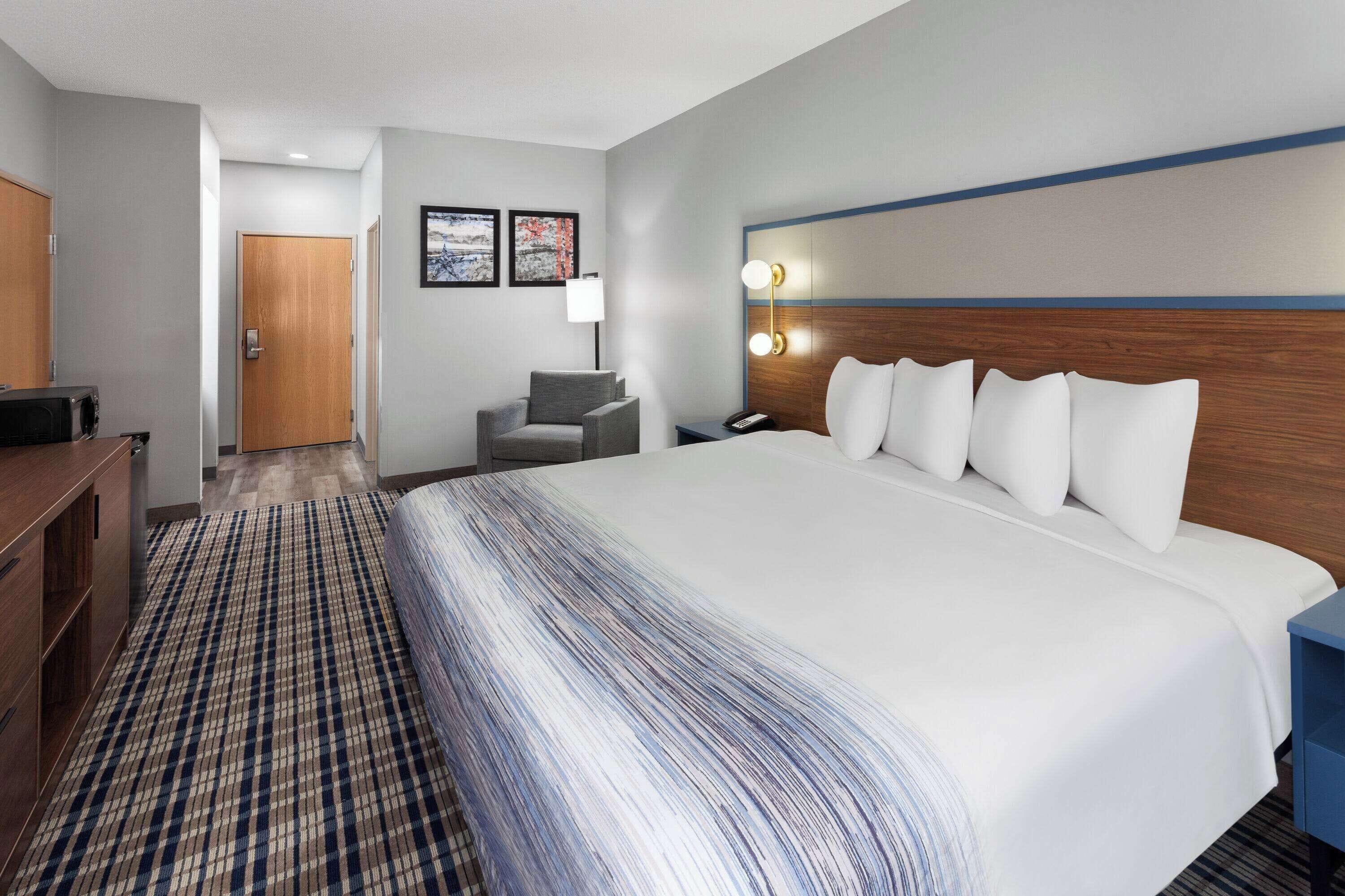 A hotel room with a large bed, a desk, a chair, a desk lamp, and a wall-mounted light fixture.