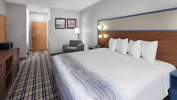 A hotel room with a large bed, a desk, a chair, a desk lamp, and a wall-mounted light fixture.