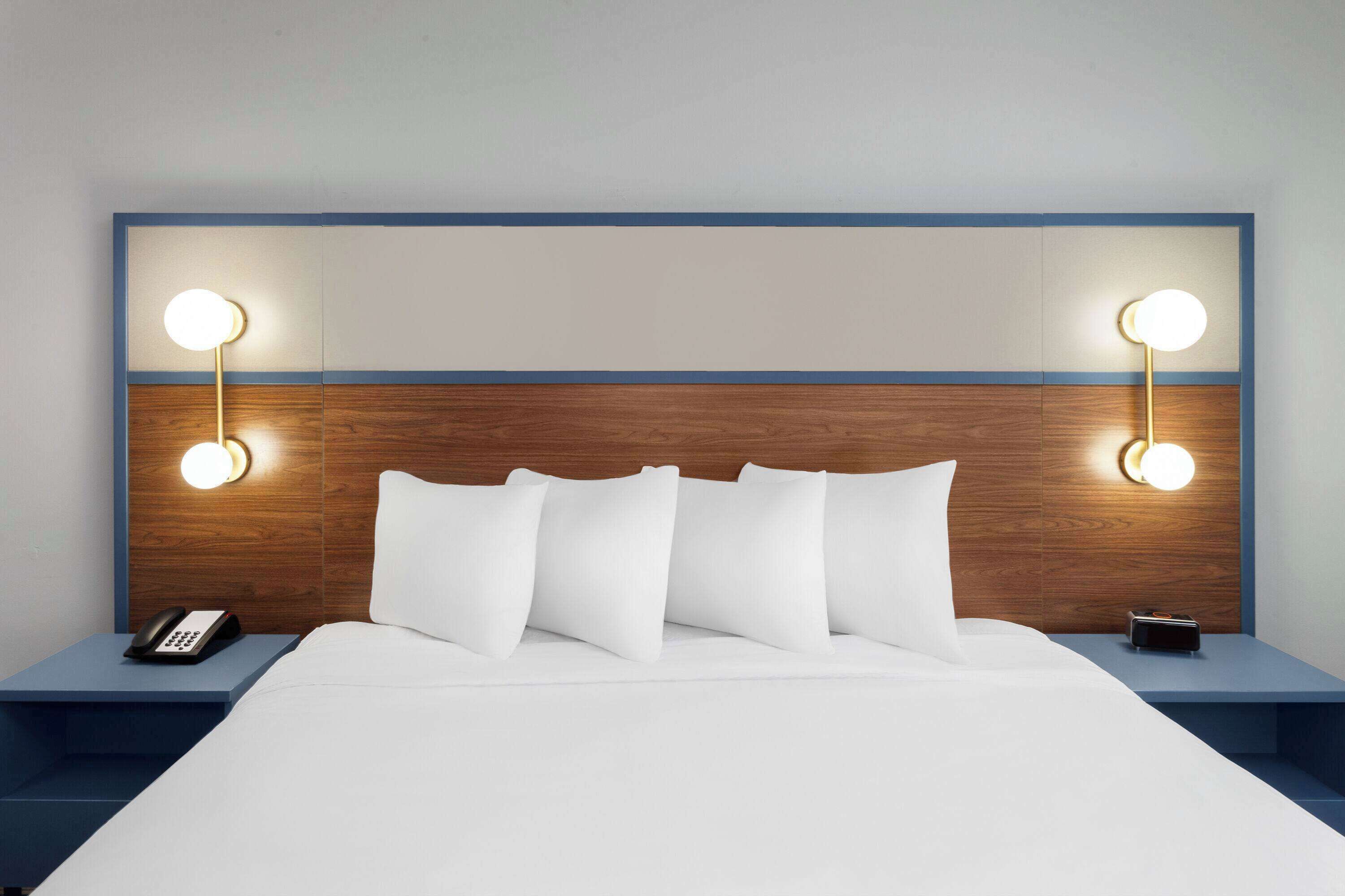 Ett hotellrum med en sänggavel i trä, vita sängkläder och sänglampor.