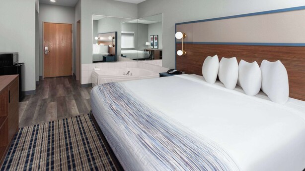 A hotel room with a large bed, a bathroom with a bathtub, a mirror, and a desk with a computer. - AmericInn by Wyndham Eagle River Downtown (Eagle River)