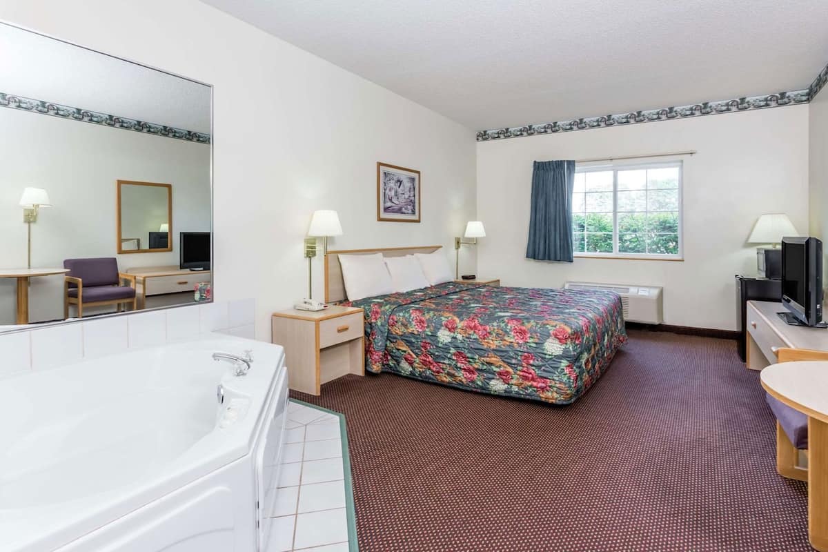 Hotelkamer met een groot bed, een zithoek met een stoel en een tafel, een grote spiegel, een raam met gordijnen en een bad.