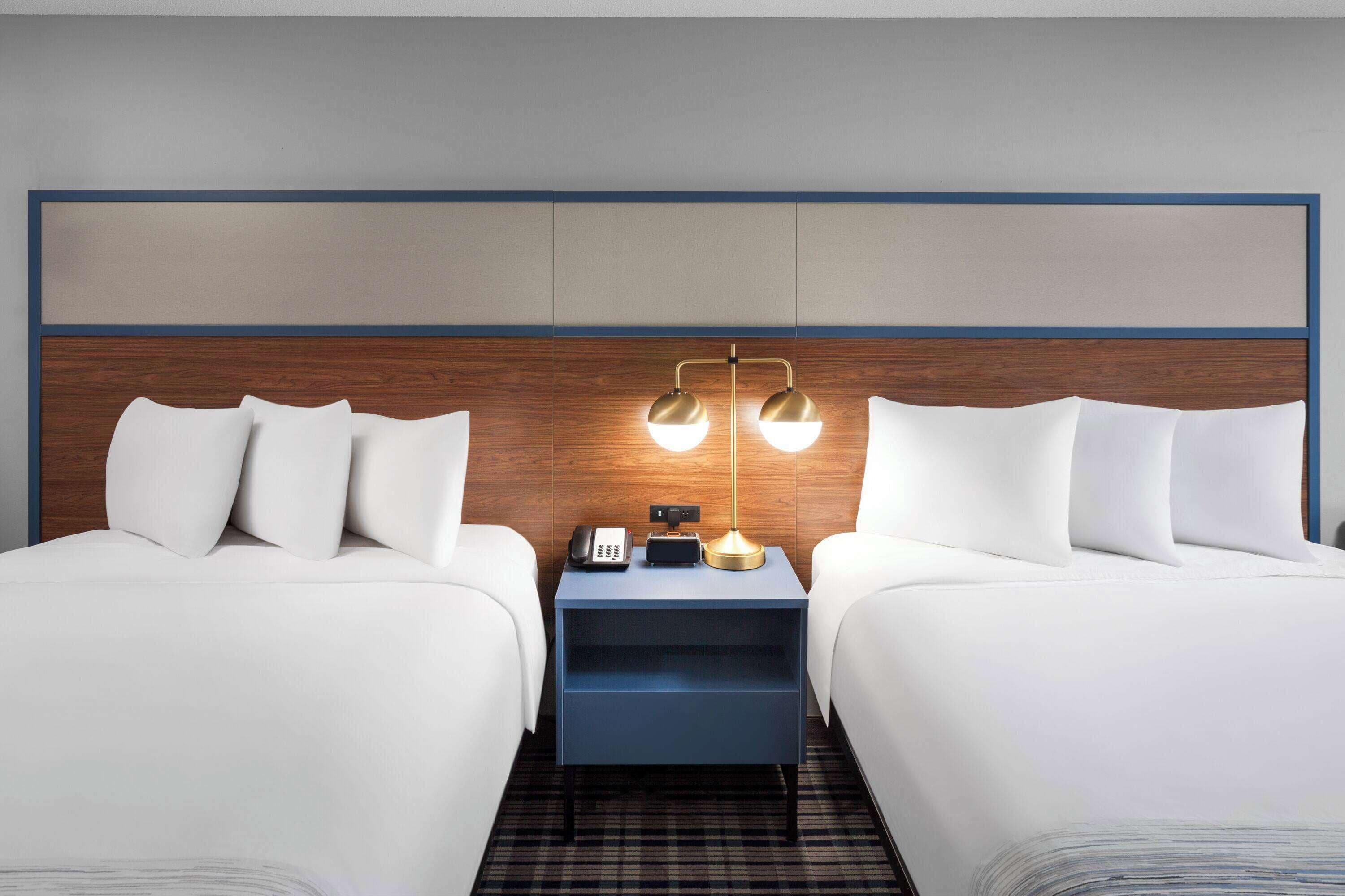 A hotel room with two beds, a nightstand with a lamp, and a phone.