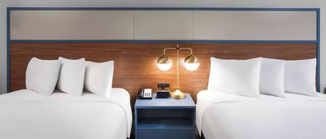 A hotel room with two beds, a nightstand with a lamp, and a phone.