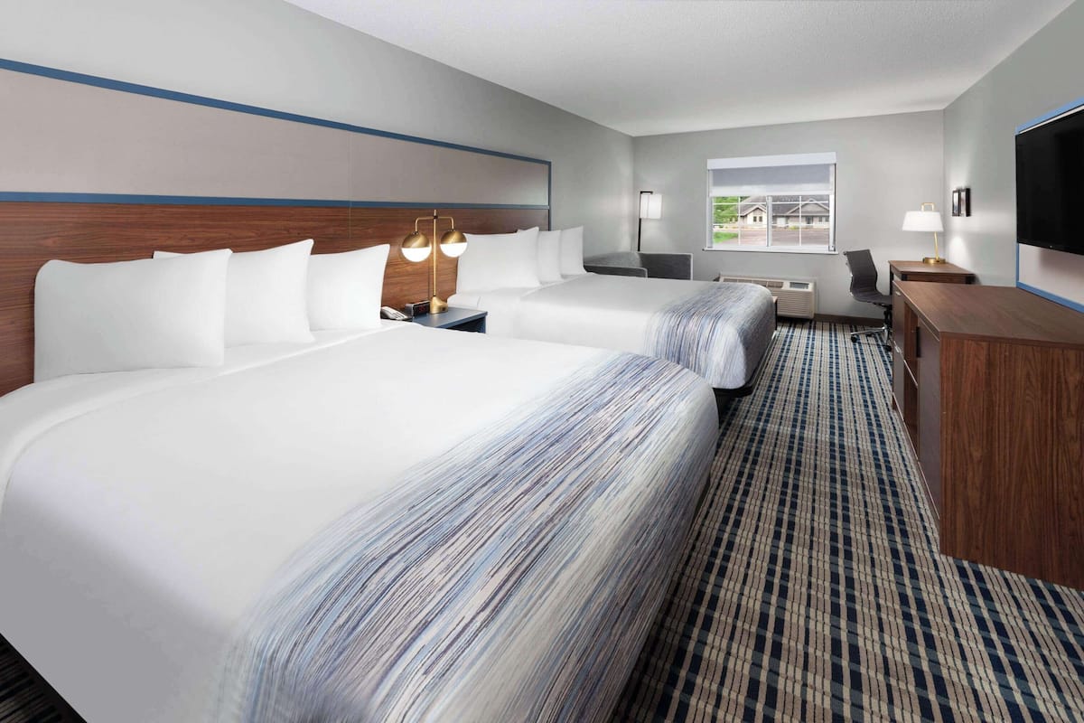Een hotelkamer met twee bedden, een bureau, een stoel, een televisie en een raam met uitzicht.