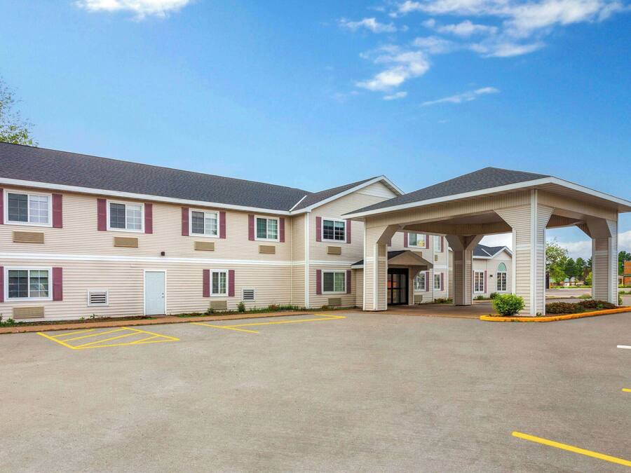 A hotel with a covered entrance, a parking lot with marked spaces, and a building facade with windows and shutters.