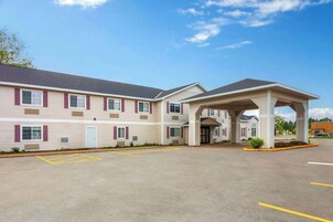 Un hotel con entrada cubierta, aparcamiento con plazas delimitadas y fachada con ventanas y contraventanas.