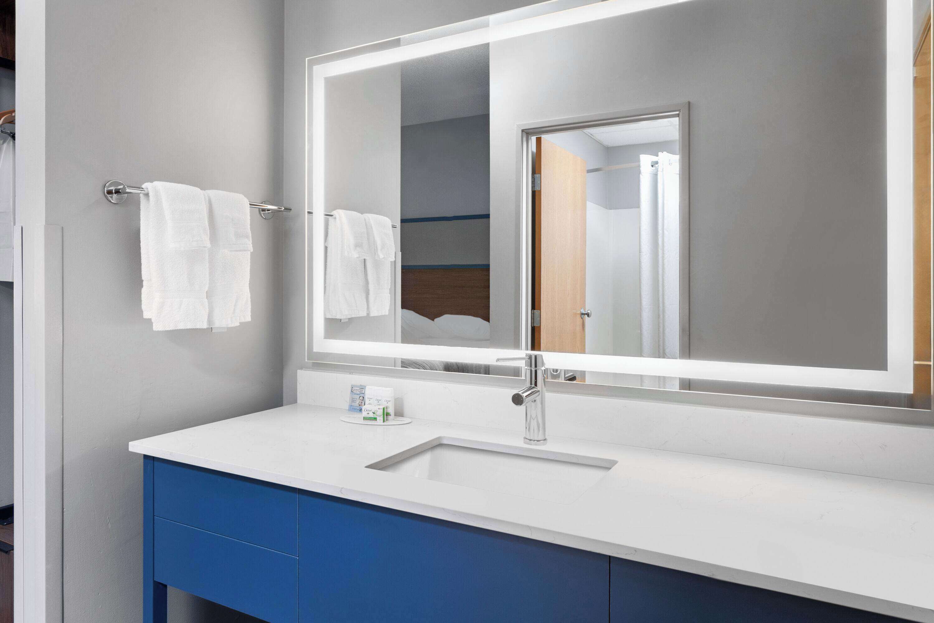 A modern bathroom with a white sink, blue cabinet, and a large mirror.