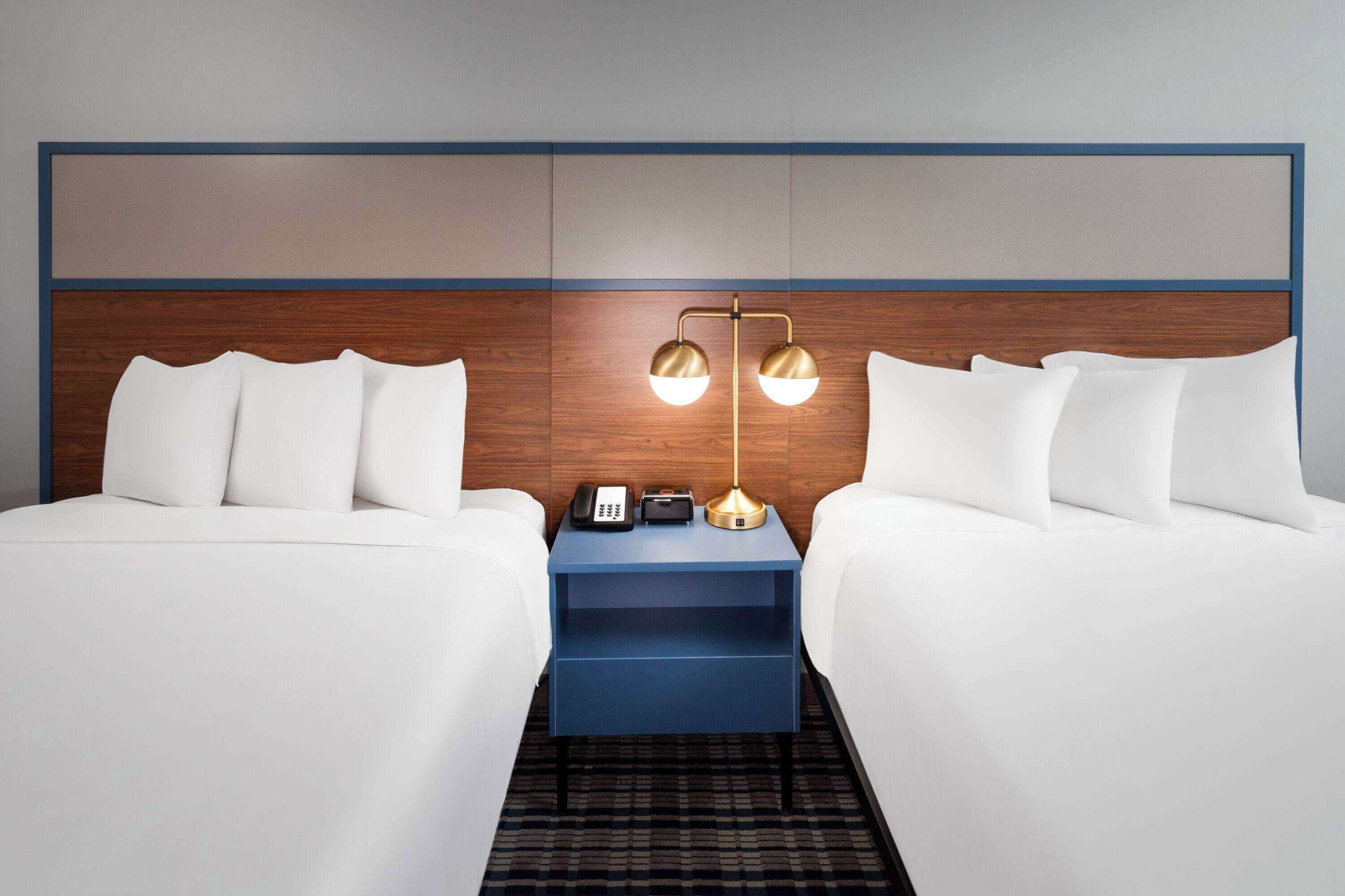 A hotel room with two beds, a nightstand, a lamp, and a telephone.