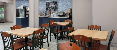 A restaurant with wooden tables and chairs, a kitchen area, and a blue-tiled backsplash.
