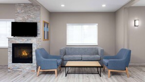 A modern living room with a fireplace, a flat-screen TV, a grey sofa, two armchairs, and a wooden coffee table. - AmericInn by Wyndham Eagle River Downtown (Eagle River)
