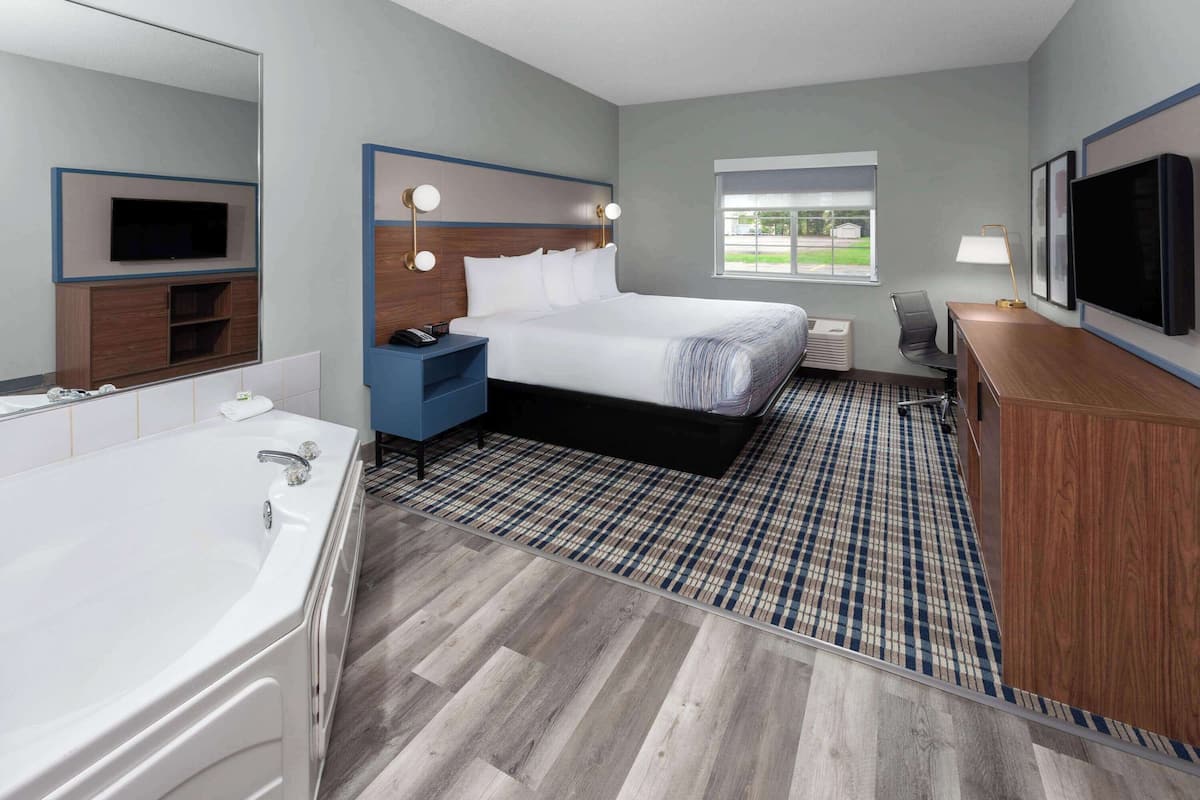 Een moderne hotelkamer met een groot bed, een aparte badkamer met badkuip, een bureau met stoel, en een aan de muur bevestigde televisie.