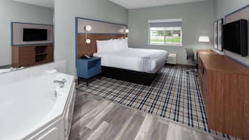 A modern hotel room with a large bed, a separate bathroom with a bathtub, a desk with a chair, and a television mounted on the wall.
