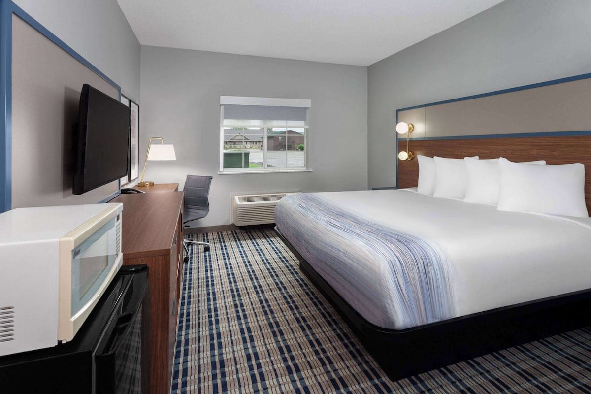 Een hotelkamer met een bed, een bureau met een televisie, een magnetron en een raam met uitzicht op gebouwen.