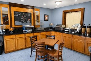 Une cuisine avec des meubles en bois, une table à manger avec des chaises, un coin café et un tableau noir décoré pour les fêtes.