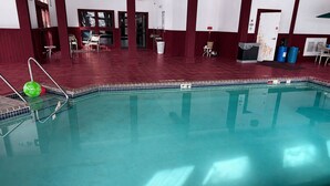 An indoor swimming pool with a tiled edge, a green ball, and a metal ladder.