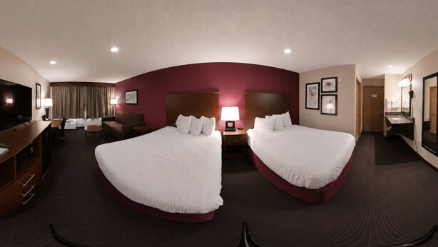 A hotel room with two beds, a TV, a desk, and a bathroom. - Coratel Inn & Suites by Jasper Black River Falls (Black River Falls)